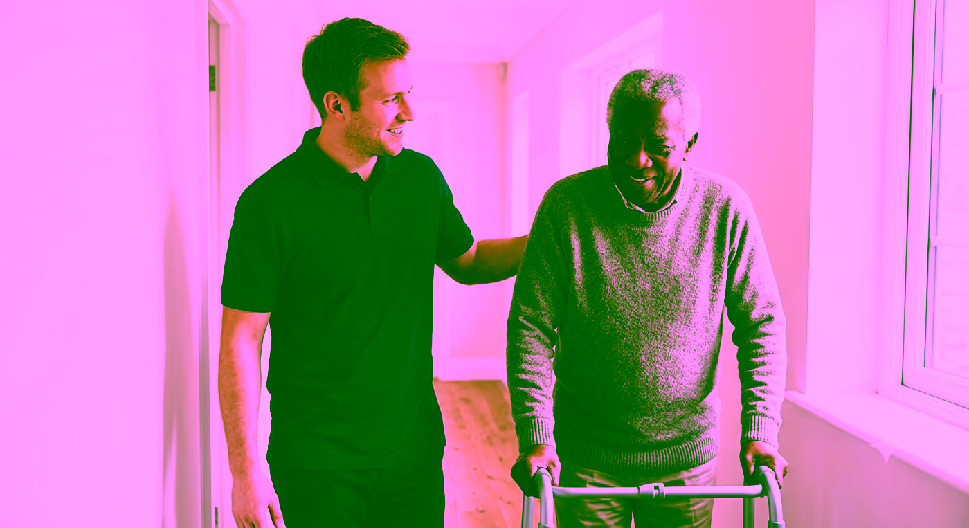 A Dendera Care carer helping an older man move safely with a walking frame