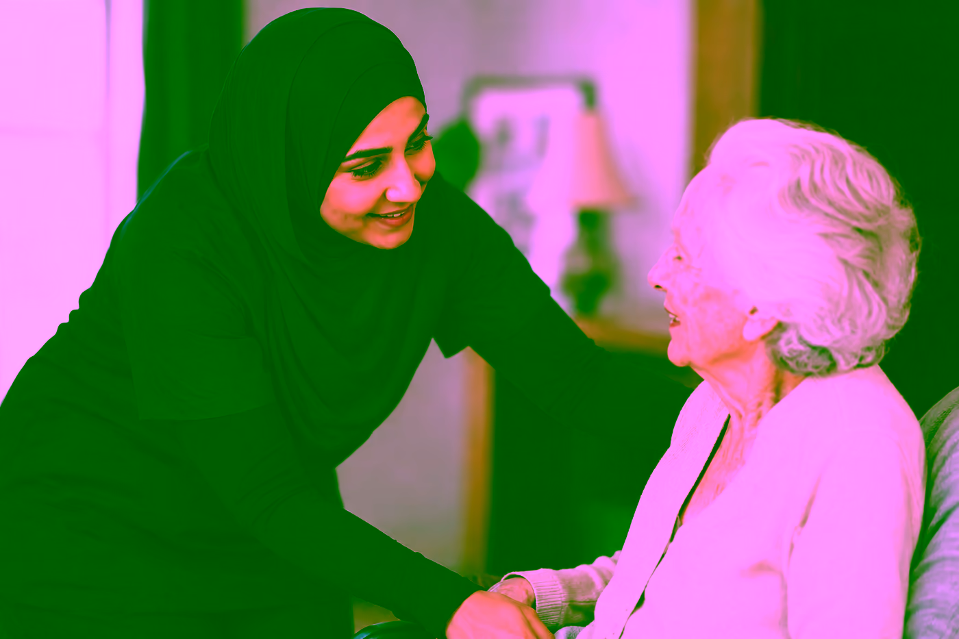 A Dendera Care carer wearing a hijab, warmly supporting an older woman at home